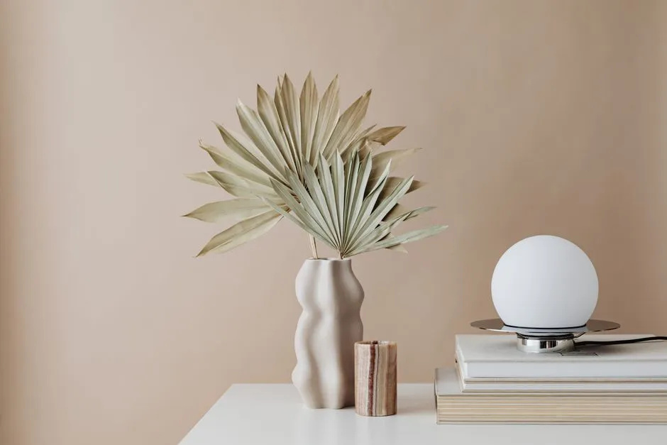 A ceramic vase and a dried palm frond in warm neutral tones